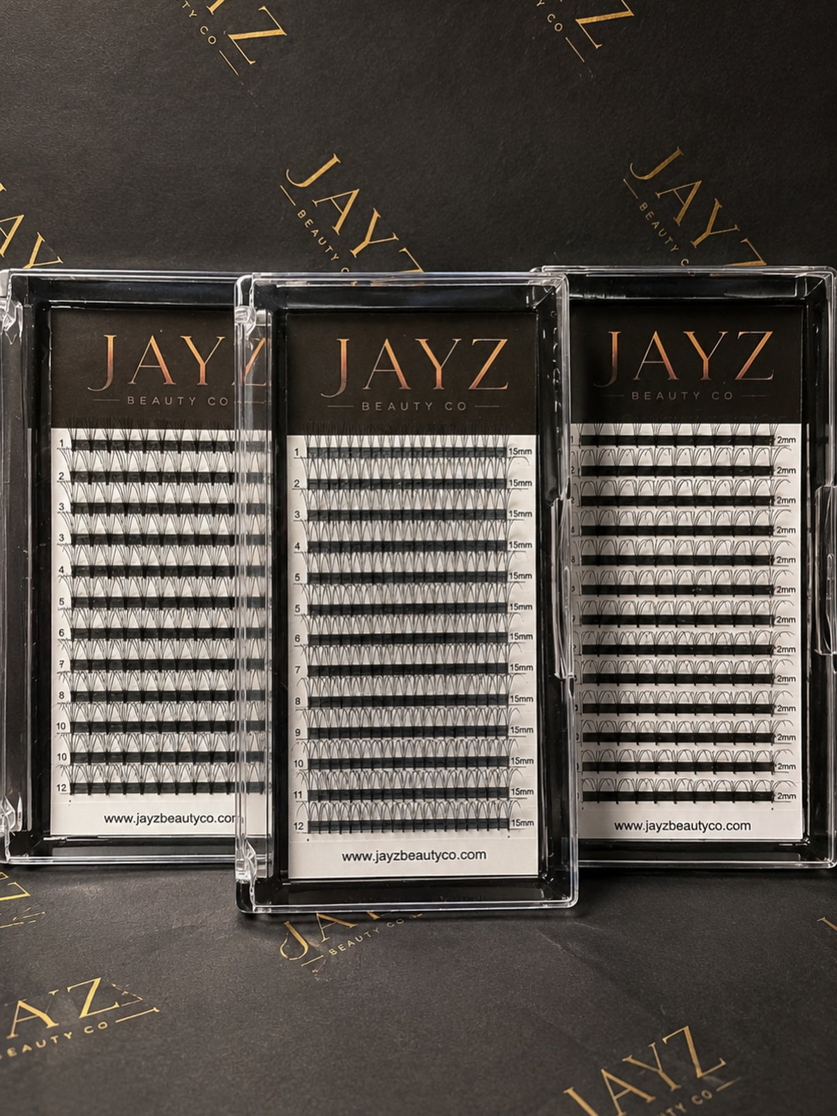 Three clear plastic trays of JAYZ Beauty Co. false eyelashes arranged on a dark branded background.